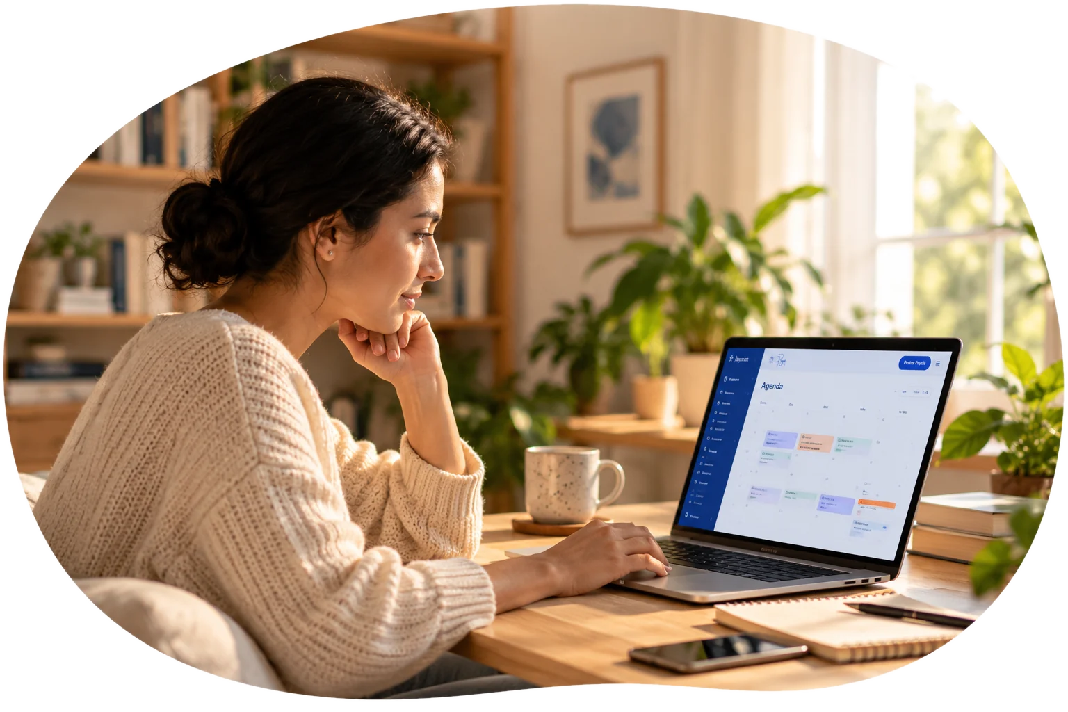 Mujer trabajando con calma en su computador portátil, en un espacio luminoso con plantas, una taza y un cuaderno.